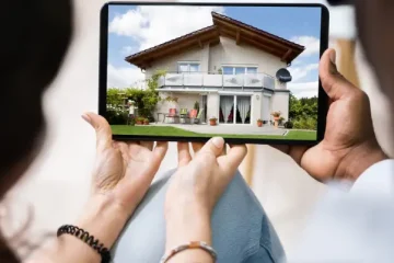 A tablet showing a two-story house viewed by people holding the device, as if inspecting real estate at home outdoor setting.