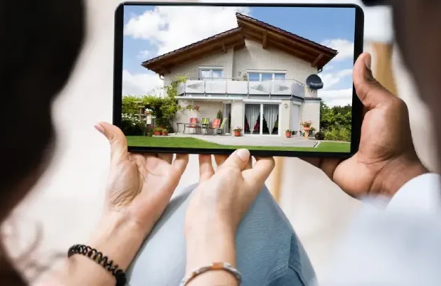 A tablet showing a two-story house viewed by people holding the device, as if inspecting real estate at home outdoor setting.