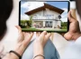 A tablet showing a two-story house viewed by people holding the device, as if inspecting real estate at home outdoor setting.