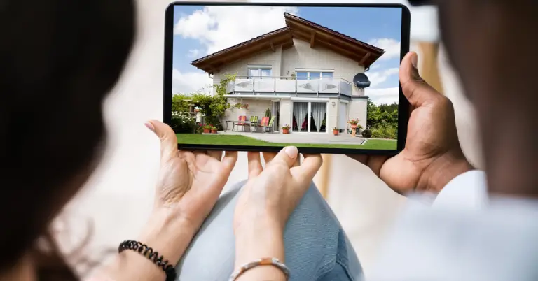 A tablet showing a two-story house viewed by people holding the device, as if inspecting real estate at home outdoor setting.