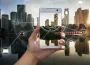Hand holding a smartphone with a city skyline and glowing connectivity graphics overlaying the scene at sunset/dusk.